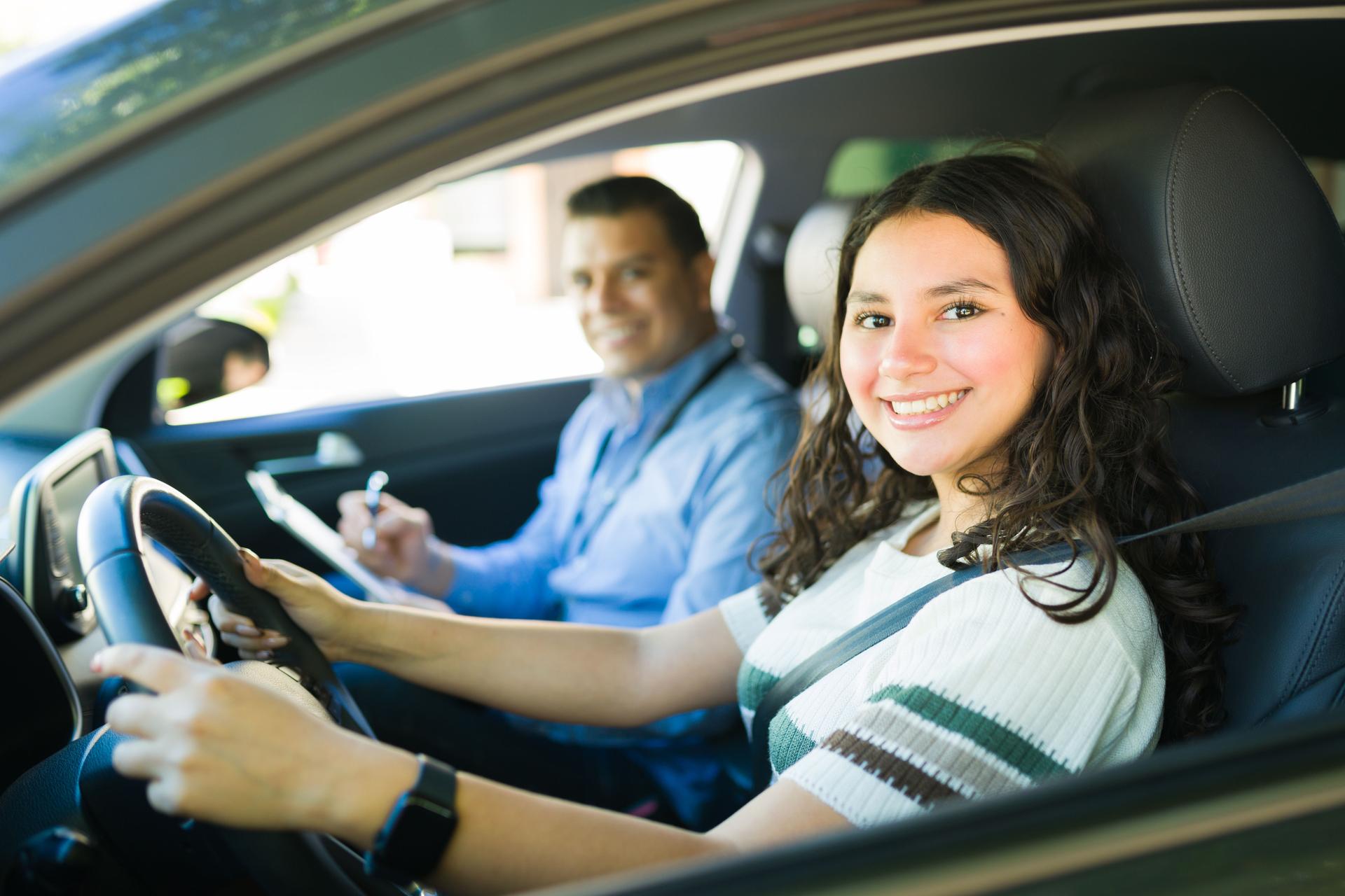 Smiling teenager learning to drive with instructor taking notes during driving lesson