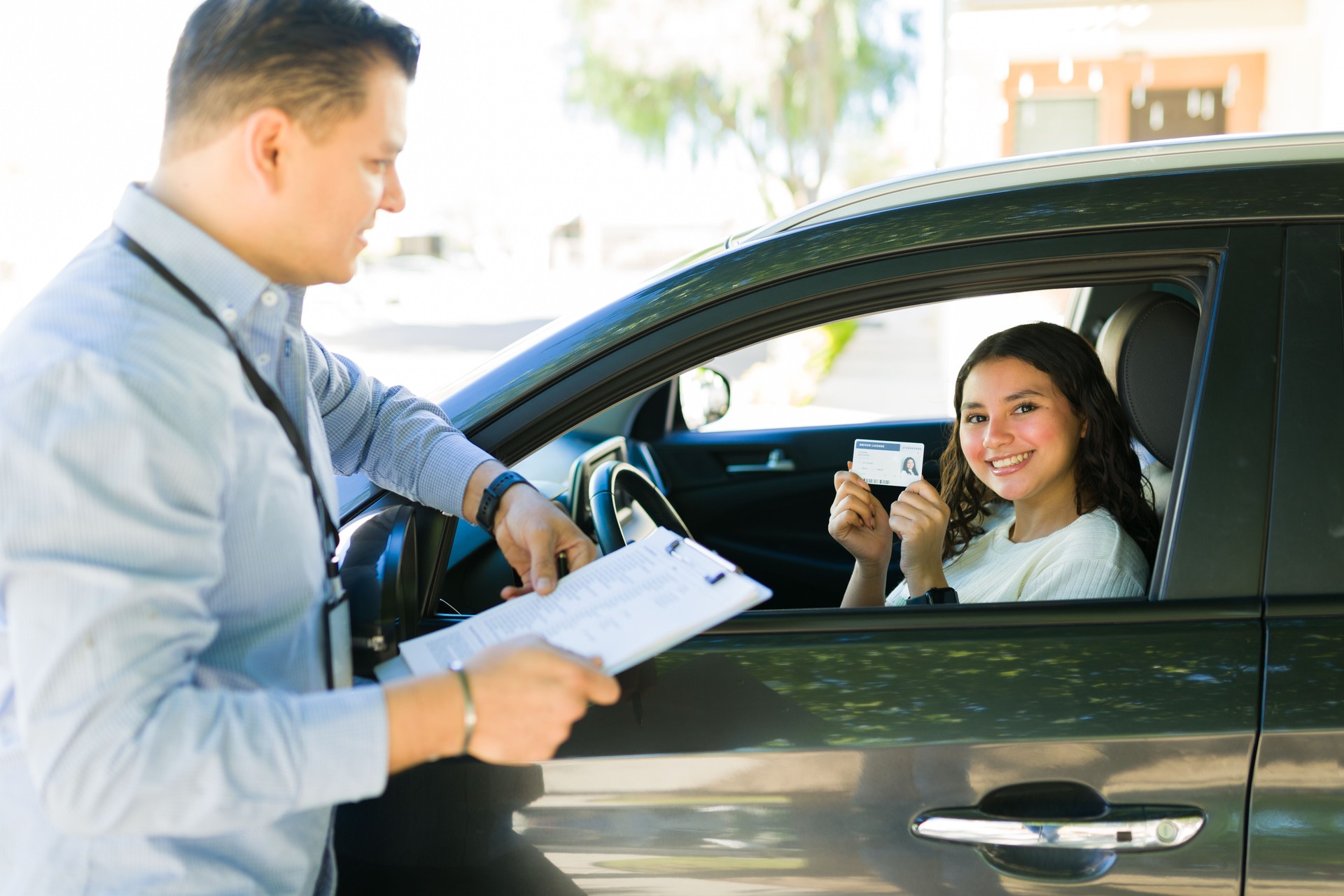 Happy teenage girl proudly displaying her driver's license to her instructor following her successful driving test