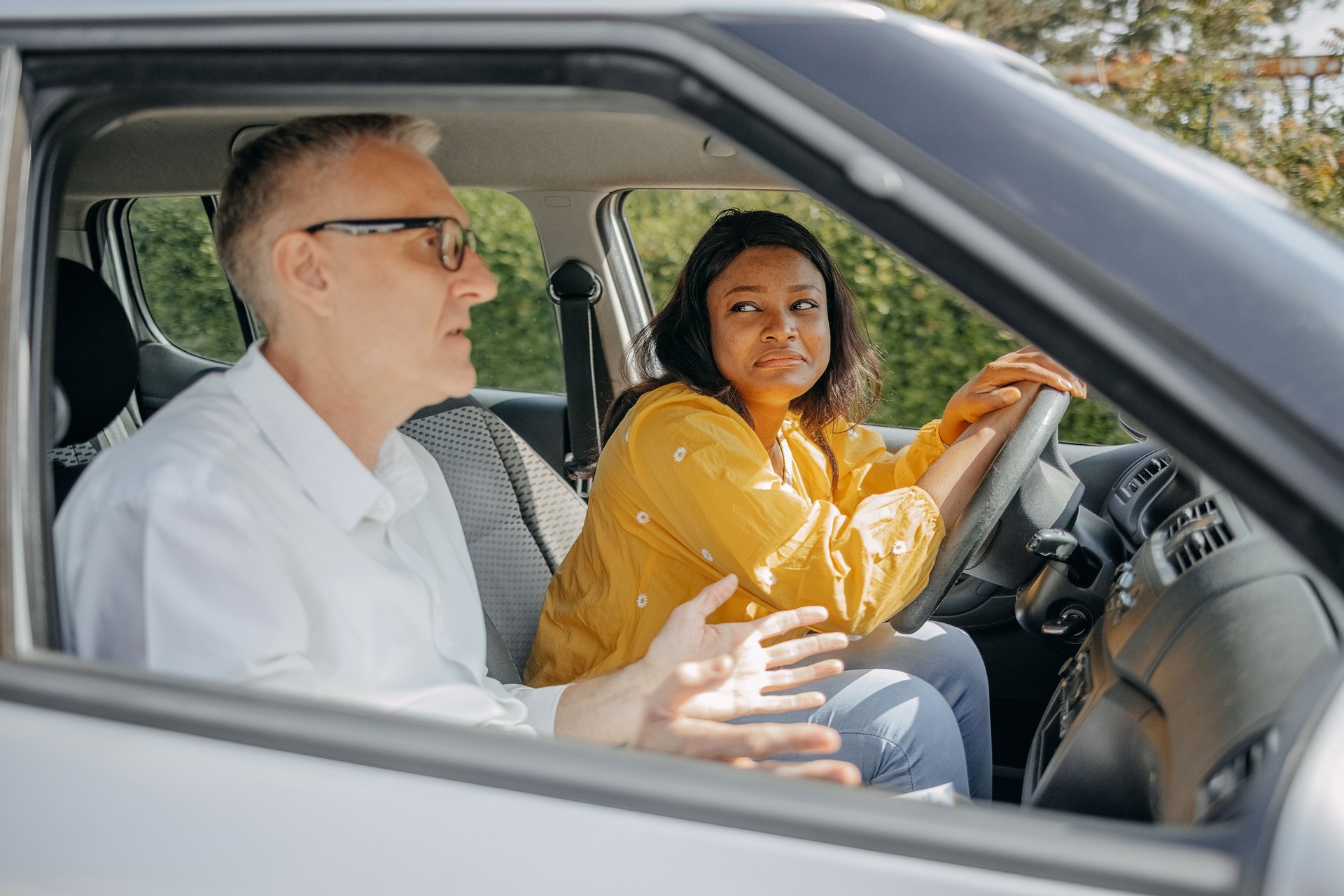 Young woman taking driving lessons with her instructor who is explaining driving basics